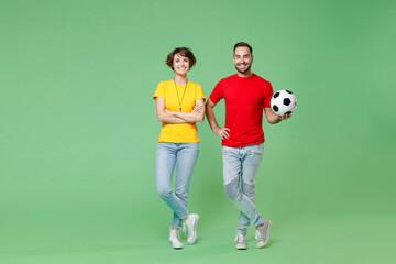 Fototapeta na wymiar Full length portrait of smiling young couple friends sport family woman man football fans in yellow red t-shirts cheer up support favorite team with soccer ball isolated on green background studio.