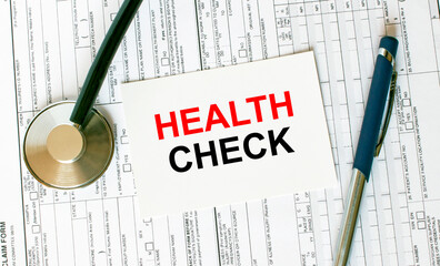 Text Health Check on the white card with the stethoscope, pen and medical documents