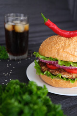 Delicious burger with red and hot peppers on top, soda in the background. Black background. advertising photo.
