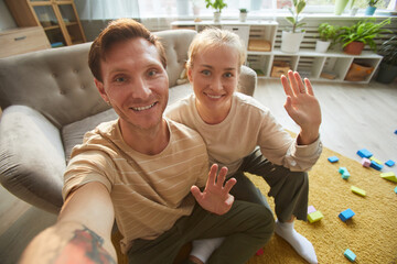 Portrait of happy young couple smiling at camera and waving sitting in the room