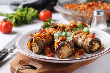 Baked eggplant rolls with chicken, onions and carrots in plate on wooden board. Horizontal format.