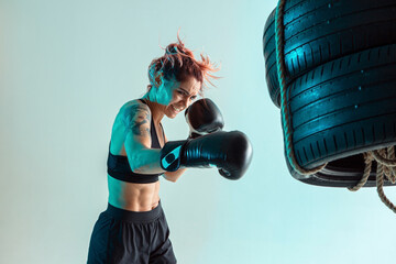 A female fighter in Boxing gloves strikes the tires with her hand