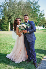 Fototapeta premium Bride and groom at wedding Day walking Outdoors on spring nature. Bridal couple, Happy Newlywed woman and man embracing in green park. Loving wedding couple outdoor. Bride and groom