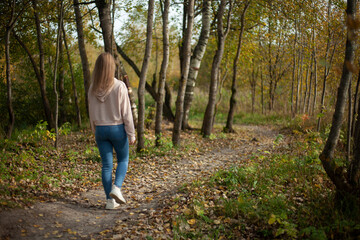 The girl walks along the path in the forest. Autumn walk in nature.