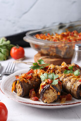 Baked eggplant rolls with chicken, onions and carrots in plate on gray background. Vertical format.