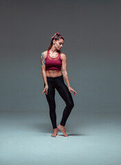 Fototapeta na wymiar Young female dancer in sportswear posing in studio on gray background