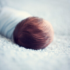 Newborn baby hairy head. Toddler in wrap. Blue wool blanket. Just born baby wrapped sleeping head detail
