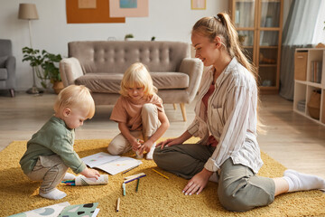 Happy young mother sitting on the floor and drawing together with her two sons in the living room