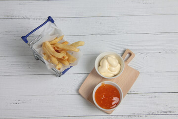 shopping cart of french fries and two bowls of sauce on wooden table flat lay