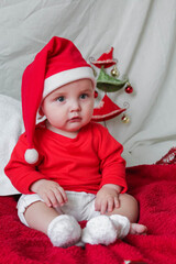 A beautiful little child is celebrating Christmas. New year holiday. Baby in a Christmas costume is happy sitting on the floor