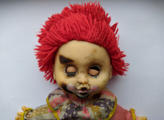 scary and old battered clown doll with burnt face and red hair on a white background