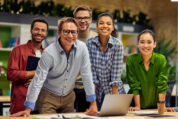 Group of young successful multi ethnic business team looking at camera and smiling while having a meeting in the modern office and coworking space