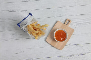 shopping cart of french fries and a bowl of sauce on cutting board on wooden table flat lay