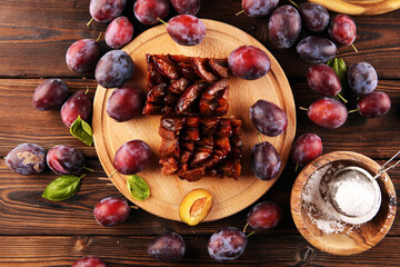 Rustic plum cake on wooden background with plums around.