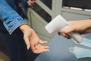 Temperature measurement by electronic infrared thermometer of a woman's hand at the entrance to a...
