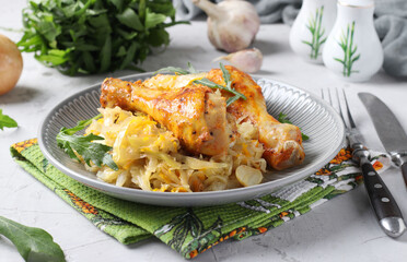 Baked chicken drumsticks with cabbage and garlic on gray plate. Closeup.