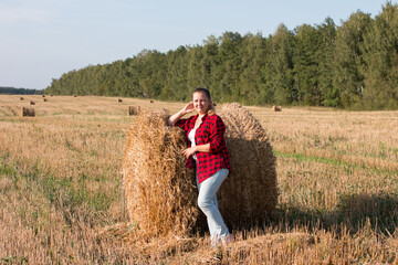 A lone woman leaned on a haystack in a field. Countryside harvesting dry grass.