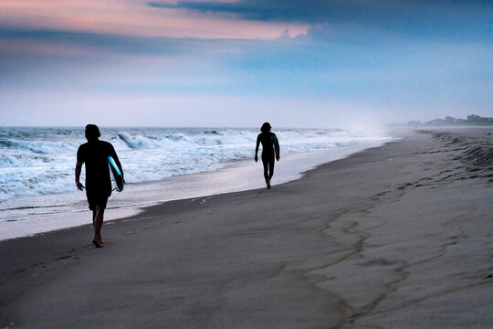 Surfers Walk On The Beach At Sunset After Surfing In The Hamptons, New York