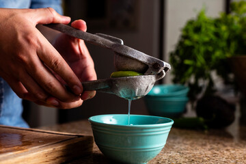 Man squeezing lime with a metal squeezer into a bowl.