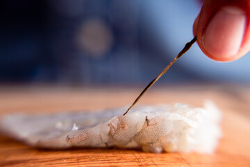 Man preparing culinary seafood, cutting raw shrimp on a wood table with a knife.