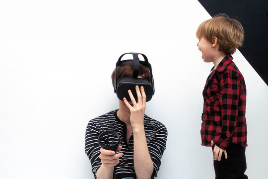 Little boy son is yelling at a young father who plays in a virtual reality glasses. Child needs attention from his father and wants to spend time at home together.