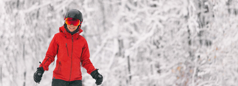 Alpine skiing skier against snow covered trees background during winter snow storm. Woman in red jacket and goggles banner landscape background.