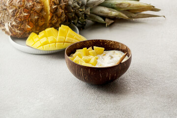 healthy breakfast consept, yogurt with fresh mango and pineapple in the coconut bowl