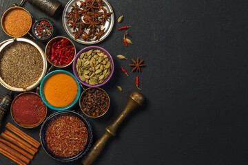 Obraz na płótnie Canvas Bright spices and fragrant dried herbs in colored bowls, copper pestle for grinding herbs on a black background. Spices for making curry.Top view, with space. Concept of national cuisine. 
