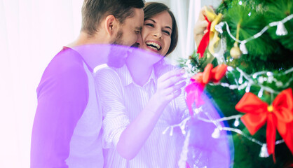 Cute excited happy couple in love are hugging each other and decorating christmas tree while winter holidays at home