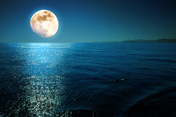Full moon with reflections on a calm sea at midnight.