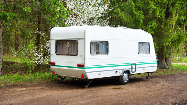 White caravan trailer in a green forest, sunny spring day. Transportation, road trip, vacations, tourism, freedom, leisure activity, lifestyle