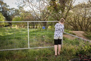 Young boy closing farm gate on country property