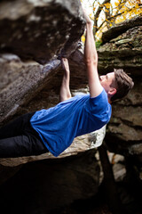 side closeup of young rock climber, bouldering on an overhang legs and hands gripping the rock .