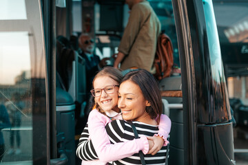 A mother hugs her daughter in front of the bus before her trip.