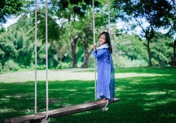little asian girl in princess costume playing wooden swing in the park