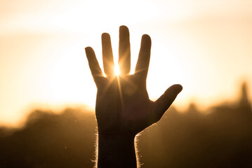 Sunset sun rays view through the fingers of an open hand with copy space, symbolizing life and hope