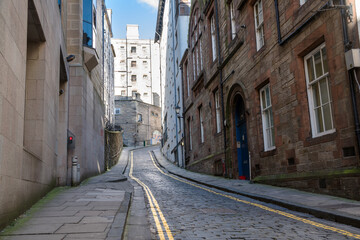 Empty narrow cobled street lined with stone buildings on a sunny winter day. Edinburgh, Scotland.