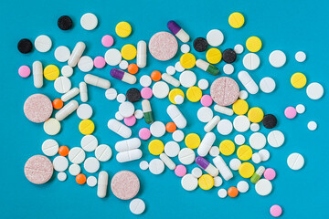 Different kinds of pills in different colors and sizes on a blue background. Top view, flat lay