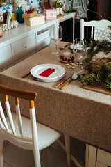 Homely christmas table setting, with pine branches rustic tablecloth in the living room of home. European style with Christmas lights.