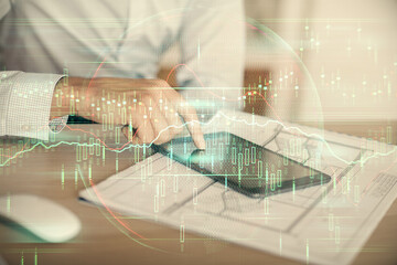 Double exposure of man's hands holding and using a digital device and forex graph drawing. Financial market concept.