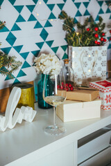 Glass of white wine next to the Christmas gifts, on the furniture in the living room. Christmas holidays