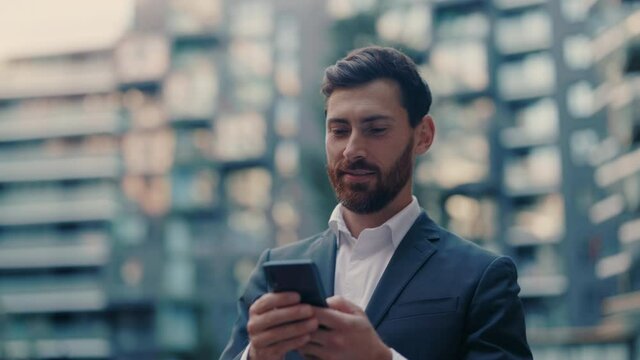Smiling young attractive businessman walking use smartphone look around at city center. Handsome man messagen stylish. Employment technology suit. Slow motion