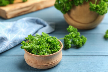 Obraz na płótnie Canvas Fresh curly parsley in wooden bowl on blue table