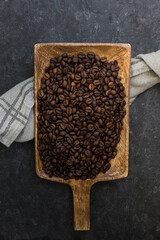 Wooden shovel full of roasted beans of coffee on a dark stone background.