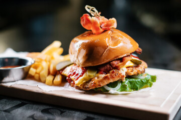 Juicy bacon burger with fries and ketchup on wooden board.