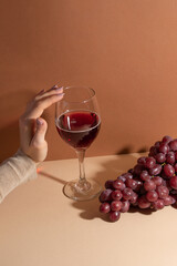 Girl's hand touch the wineglass with tasty red wine on beige. Festive concept.