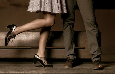 Legs of a couple standing and kissing on a wooden bench.