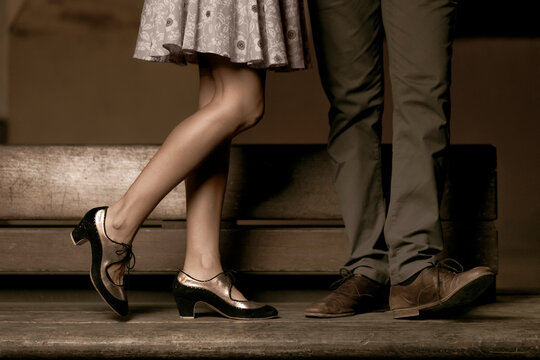 Legs of a couple standing and kissing on a wooden bench.