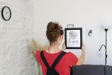 Woman arranging picture frames on wall in new house, diy home improvement concept