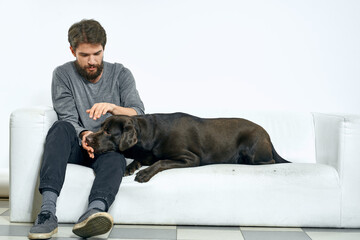 man with a black dog on a white sofa on a light background close-up cropped view pet human friend emotions fun